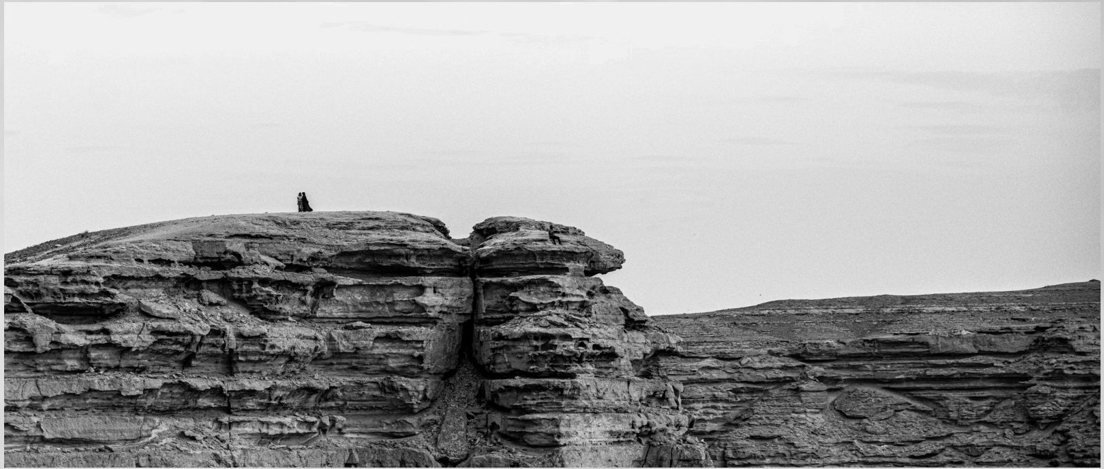 A lone figure standing on a rocky ridge above a vast landscape