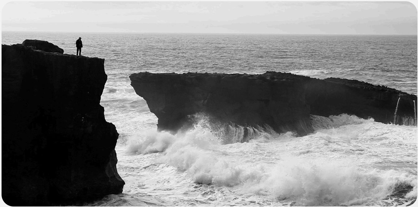 A person standing at a cliff edge above a turbulent ocean